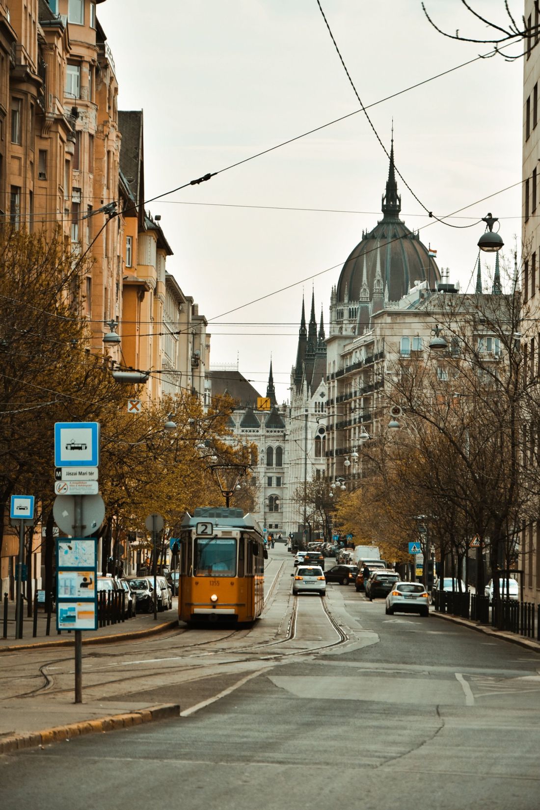 A yellow number 2 tram on a tree-lined Budapest street, with the dome of the Hungarian Parliament behind